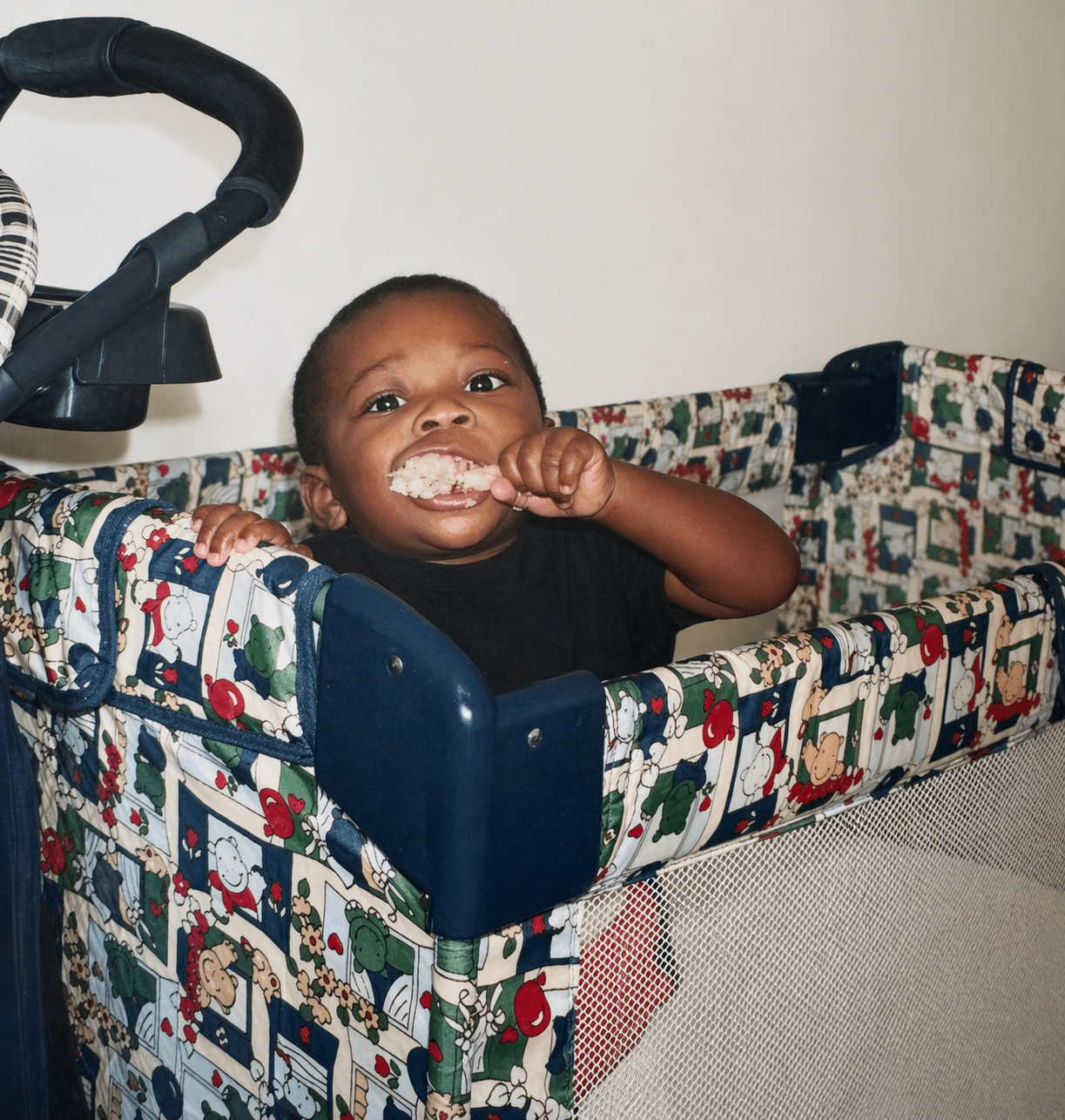 Daniel as a baby in a playpen, mid-bite on a chicken leg, staring directly at the camera